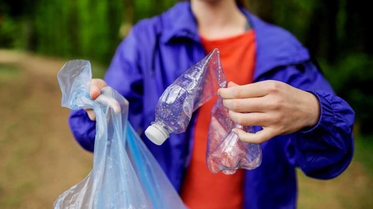 Person placing a plastic bottle into a plastic trash bag.