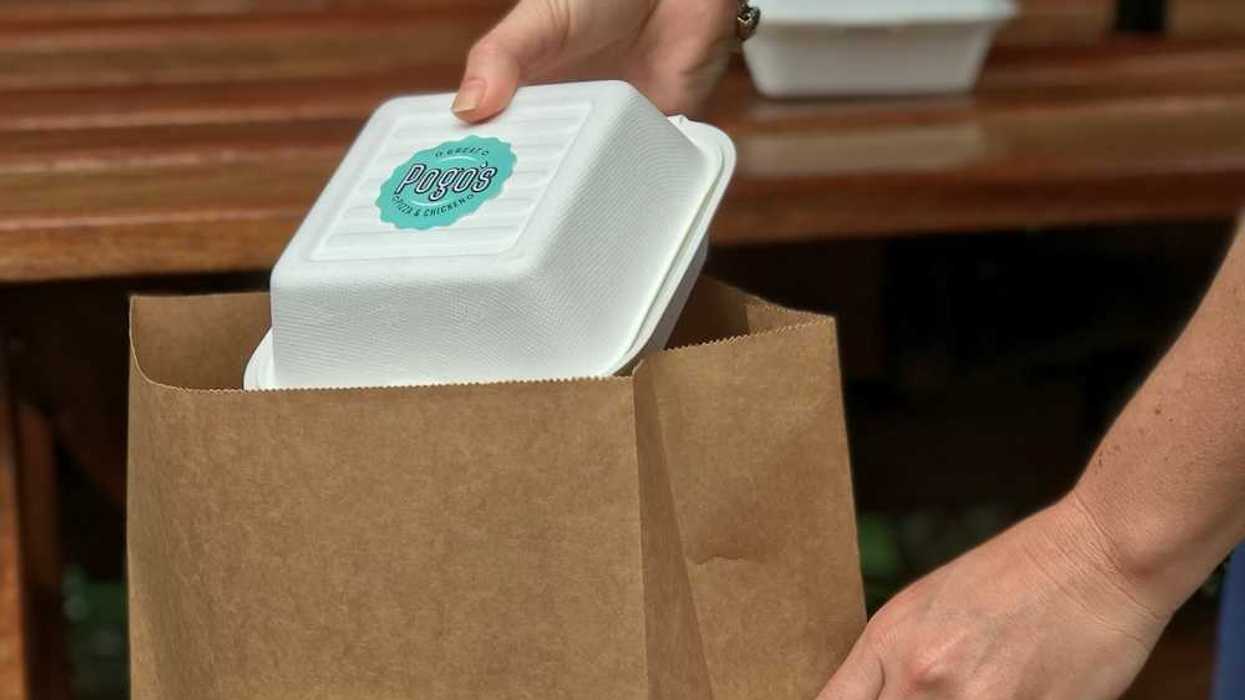 Person placing a plastic takeout container into a brown paper bag