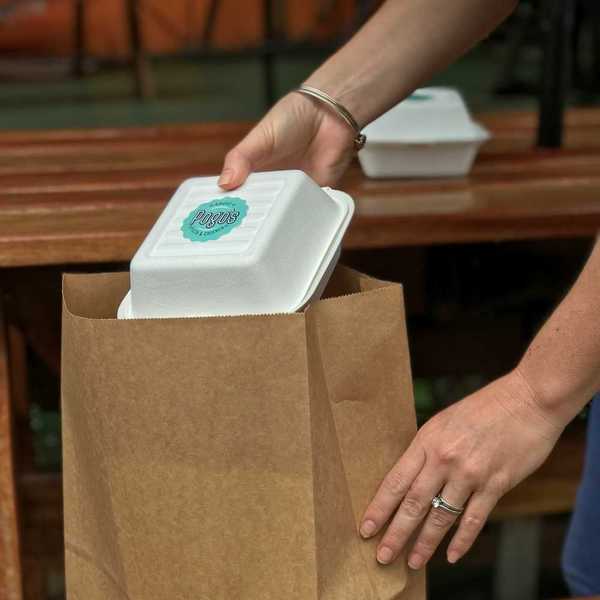 Person placing a plastic takeout container into a brown paper bag
