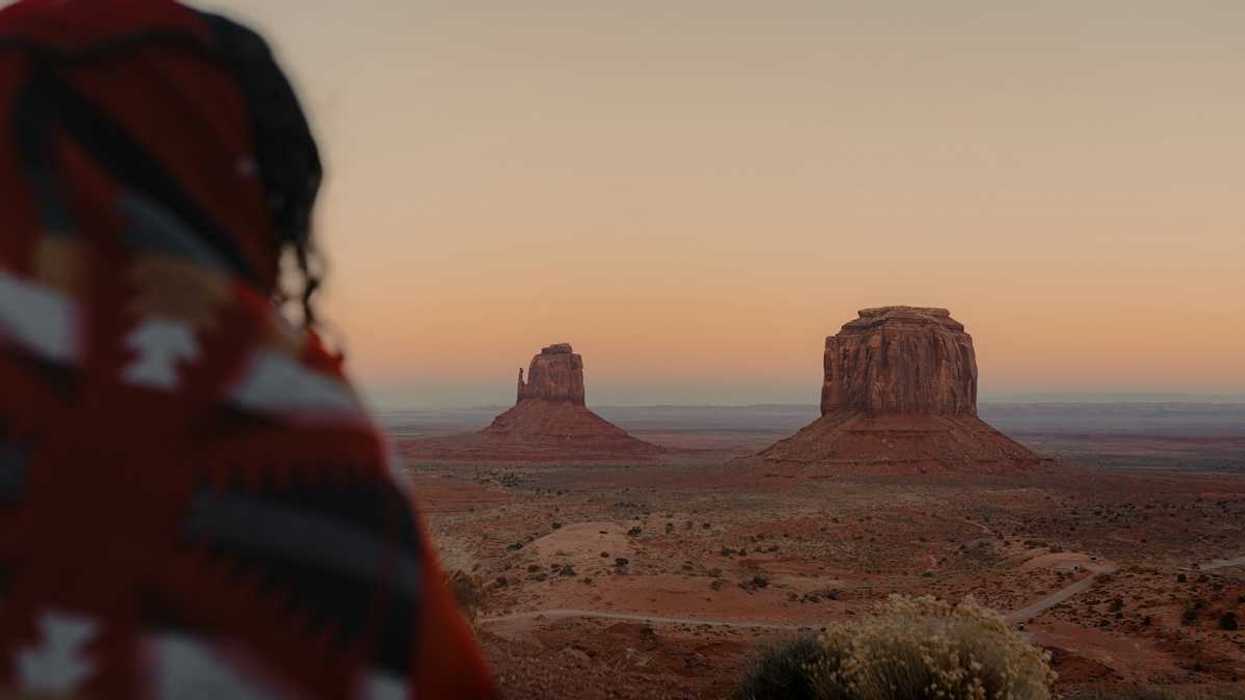 Person, presumably indigenous, facing out at Monument Valley vista.