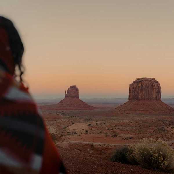 Person, presumably indigenous, facing out at Monument Valley vista.