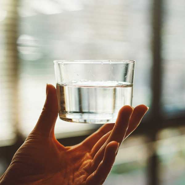 person's hand holding clear glass cup with half-filled water.