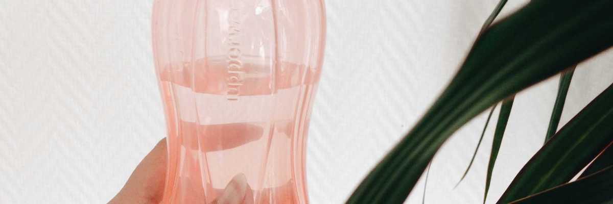 person's hand holding pink plastic water bottle.