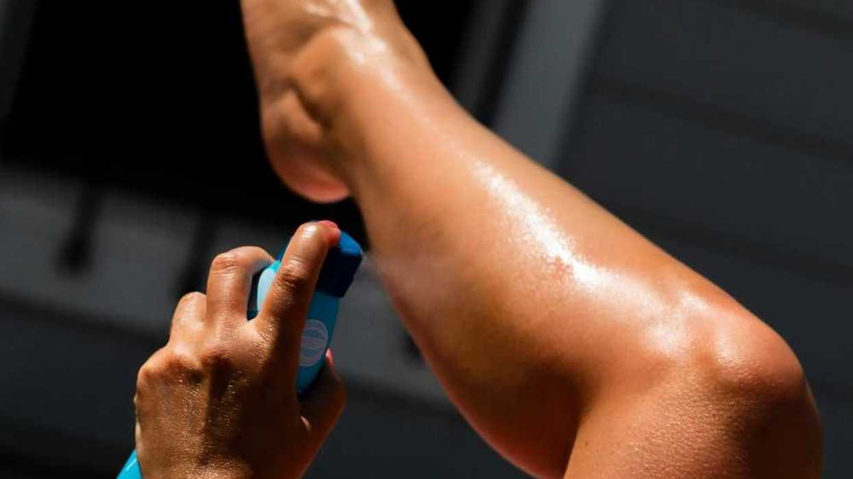 Person spraying sunscreen on left calf using left hand