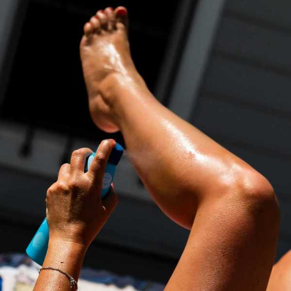 Person spraying sunscreen on left calf using left hand