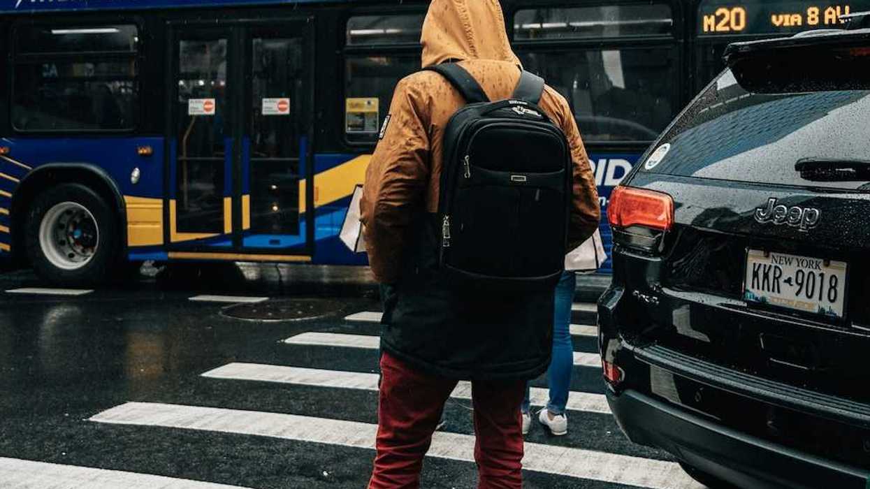 Person standing on curb at crosswalk with a "clean-energy bus" in the background