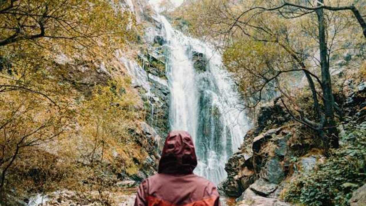 Person wearing a red rain jacket facing a waterfall