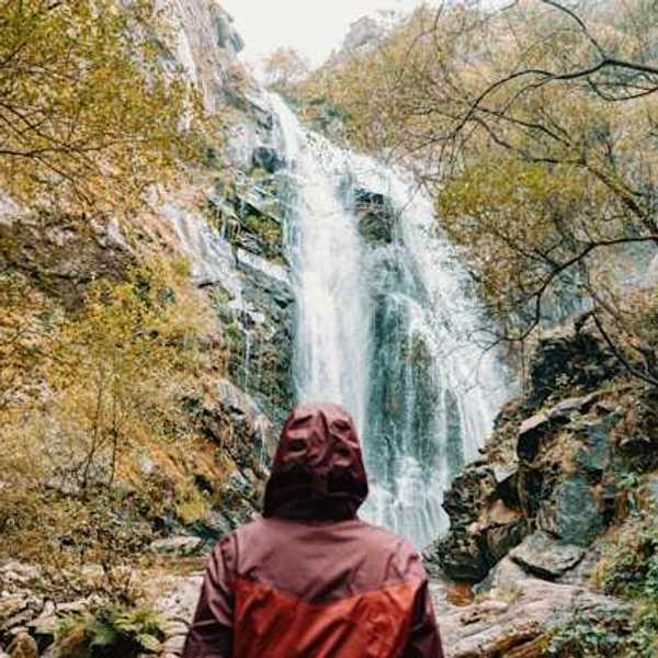 Person wearing a red rain jacket facing a waterfall