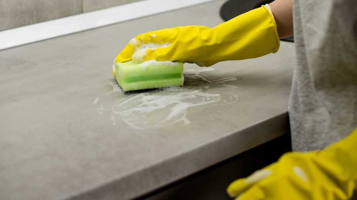 Person wearing yellow protective gloves scrubbing a countertop with a sponge.