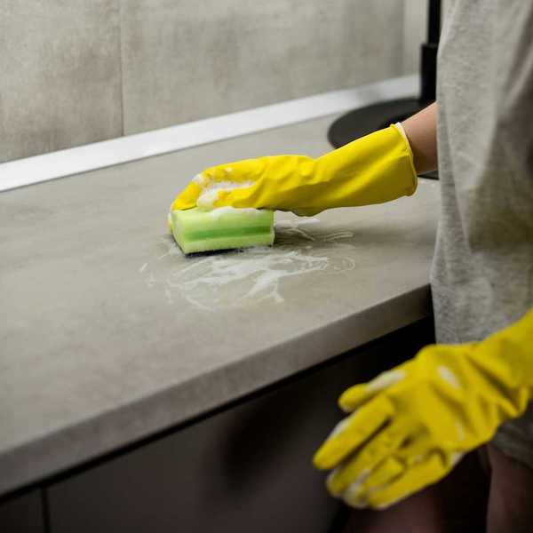 Person wearing yellow protective gloves scrubbing a countertop with a sponge.