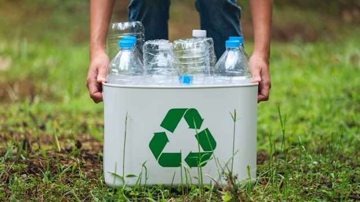 Person with a metal recycling bin carrying plastic bottles