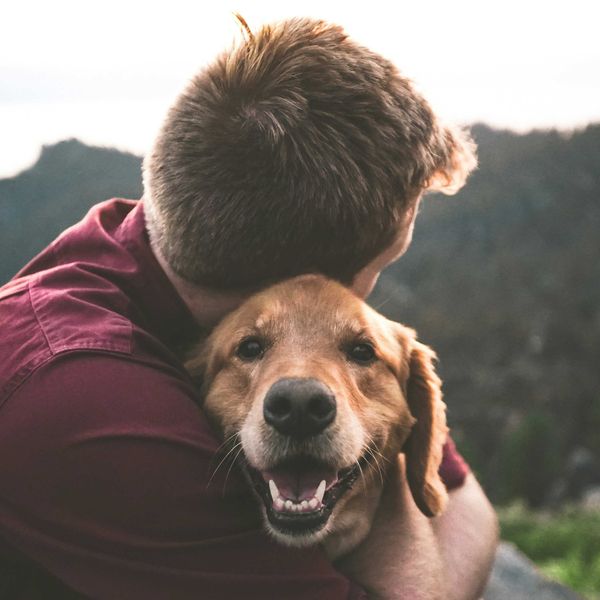 photo of man hugging a smiling tan dog.