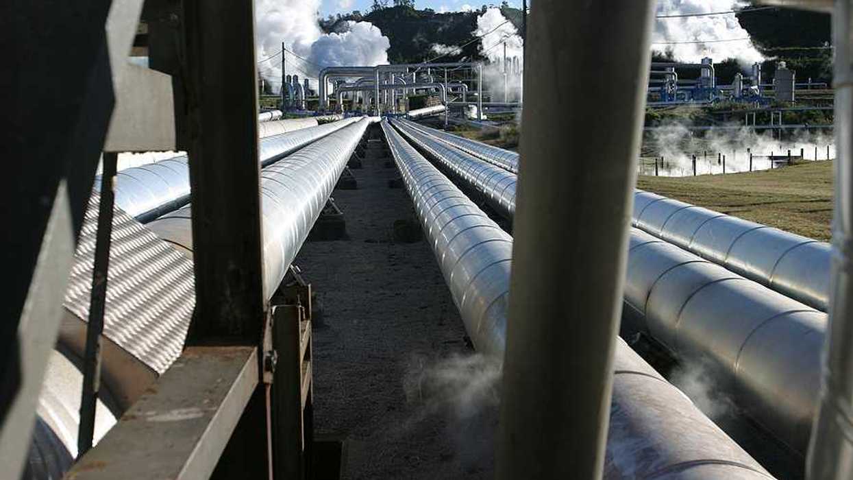 Pipelines extending toward a geothermal energy plant with steam rising from it