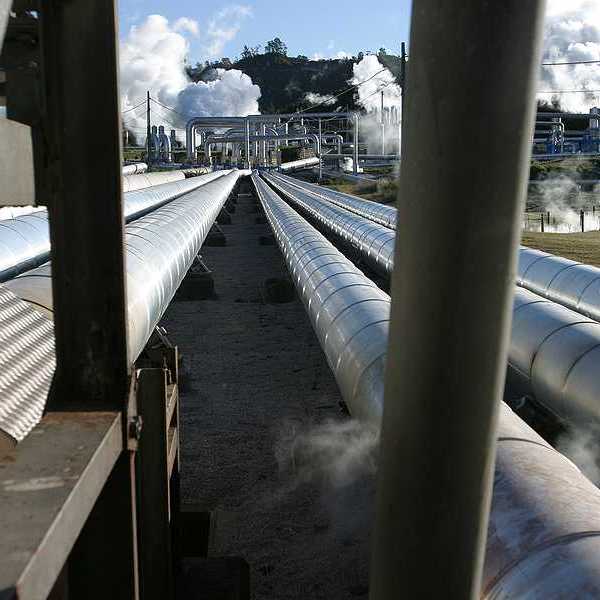 Pipelines extending toward a geothermal energy plant with steam rising from it