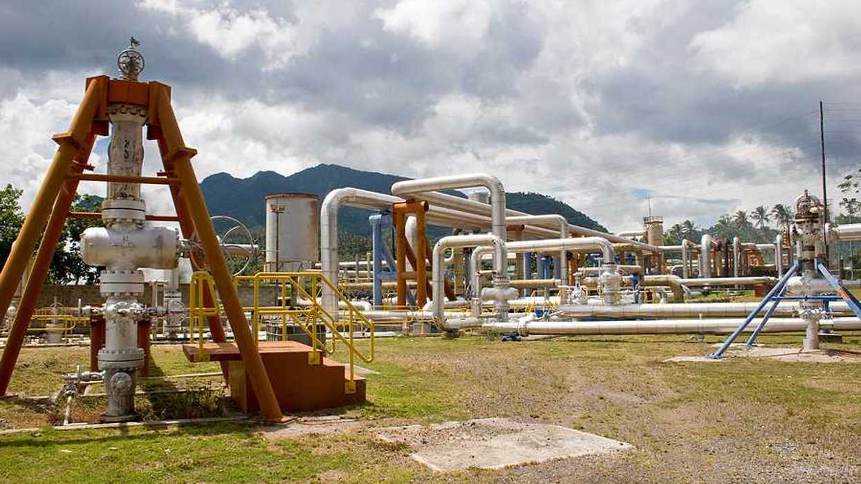 Pipes rising out of the ground at a geothermal well with mountains in the background