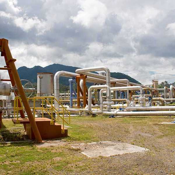 Pipes rising out of the ground at a geothermal well with mountains in the background