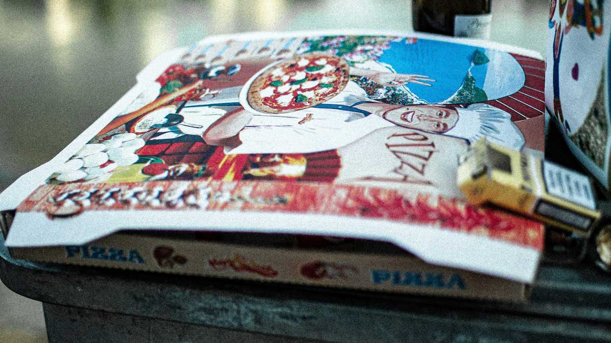 pizza box and bottle of wine outdoors with body of water in background.