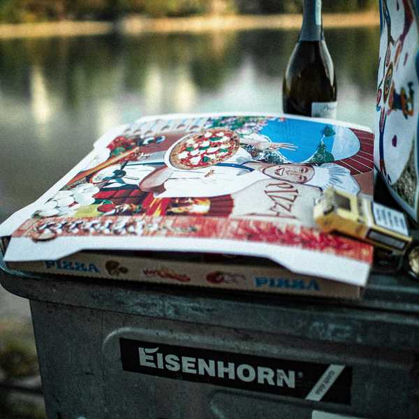pizza box and bottle of wine outdoors with body of water in background.