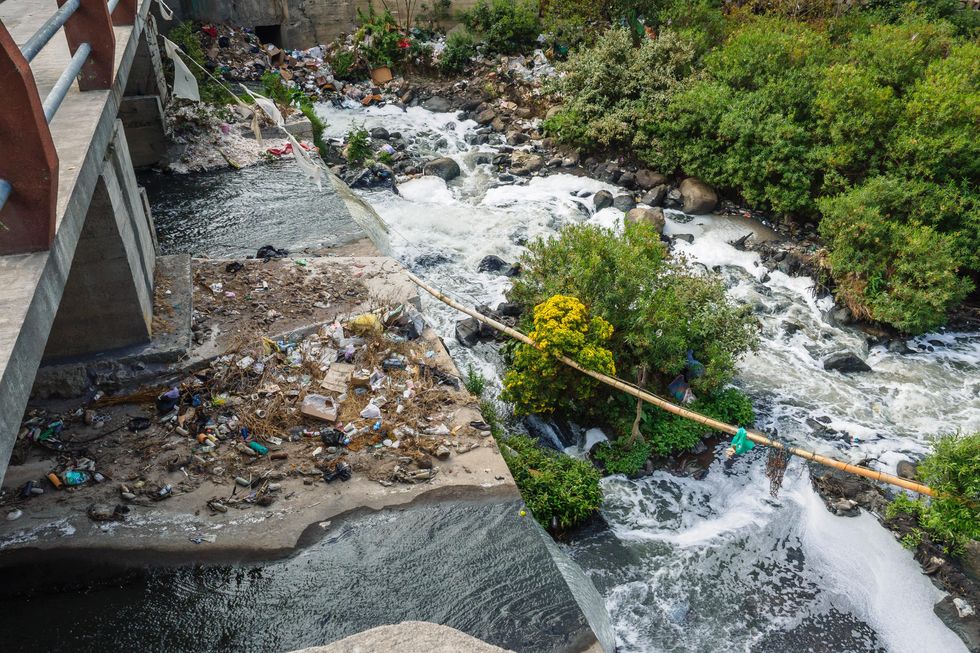 plastic trash dumped in a river under a bridge.