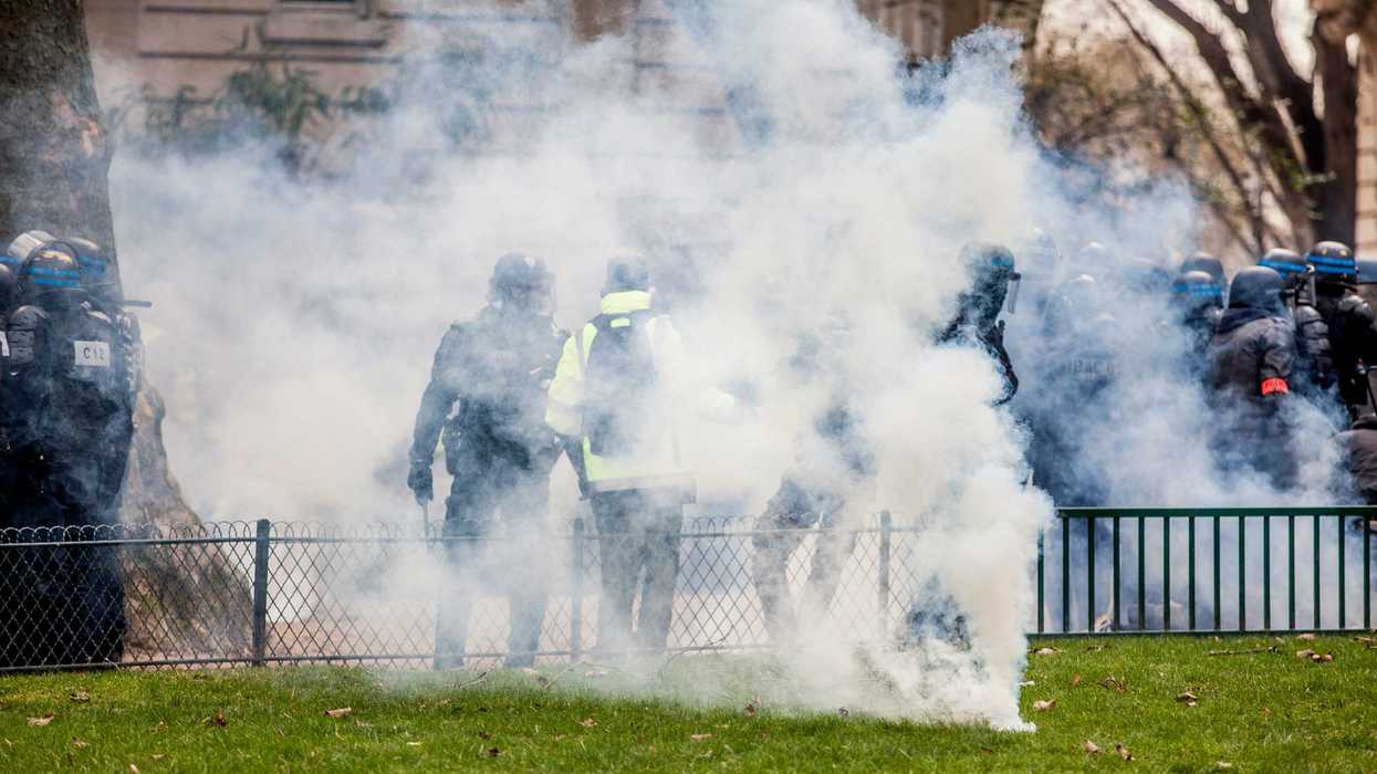 policemen throwing teargas on green grass field.