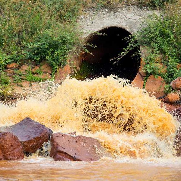 Polluted orange water coming from a pipe and entering a river