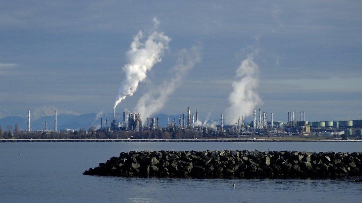 Pollution emissions billow from smokestacks along a body of water.