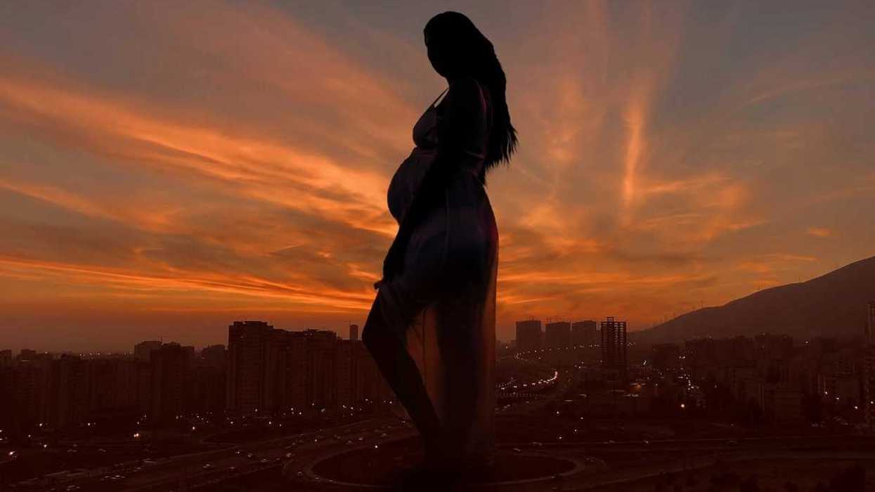 Pregnant woman against an urban backdrop and sunlit, semi-dark skies