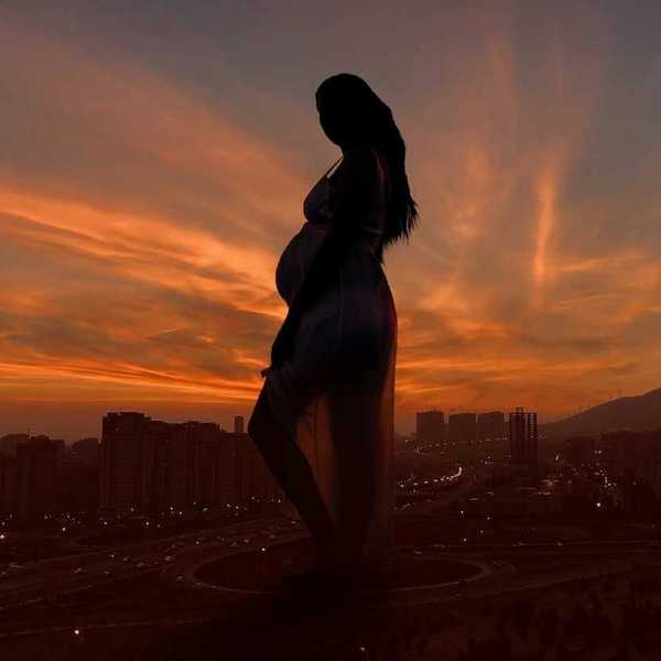 Pregnant woman against an urban backdrop and sunlit, semi-dark skies