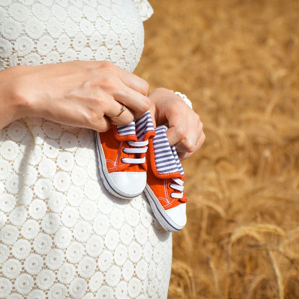 Pregnant woman holding two red baby shoes to her belly.