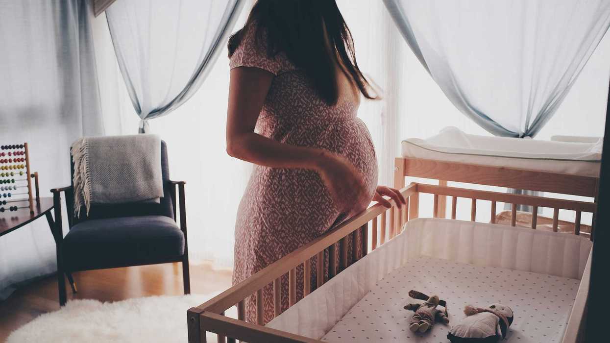 pregnant woman in a dress standing beside brown wooden crib.