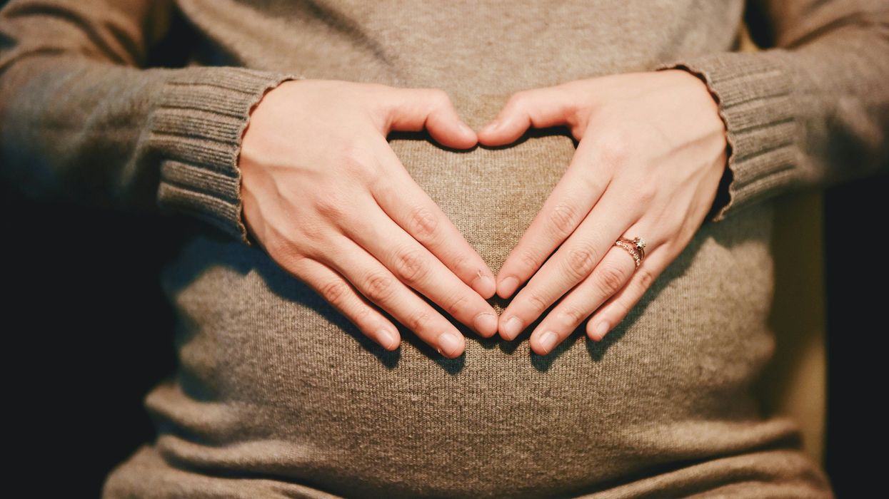 Pregnant woman wearing a beige sweater with hands on belly.