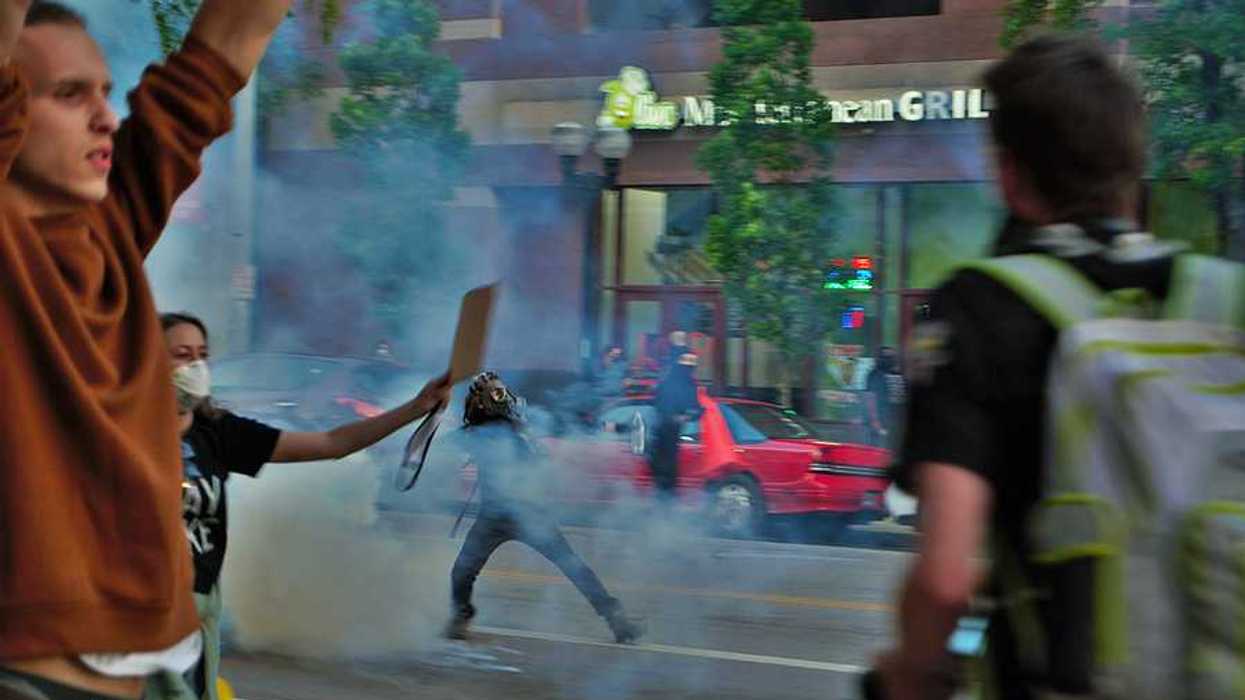 Protesters running through a street with tear gas smoke