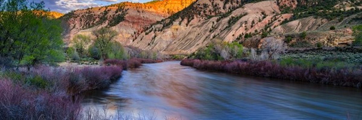 Red and beige hillsides over a swift creek or river.