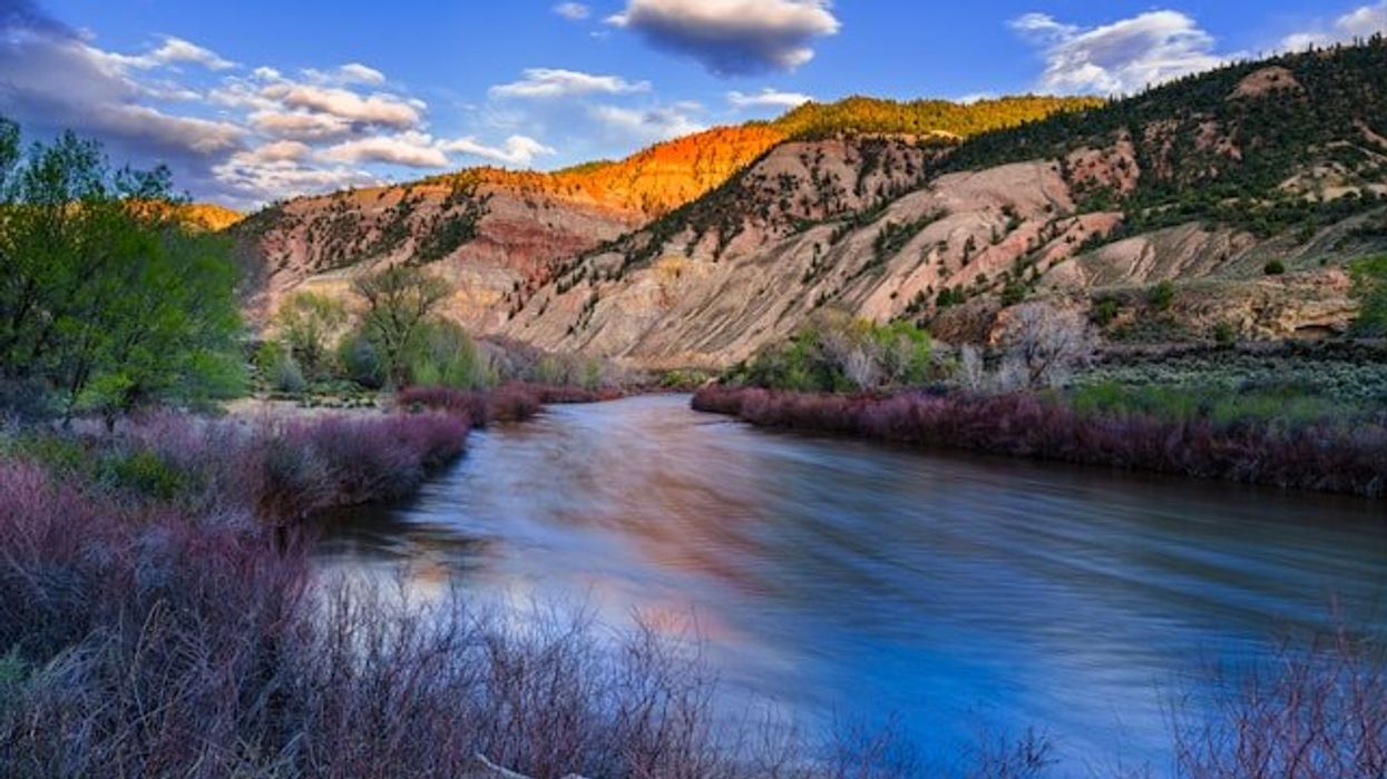 Red and beige hillsides over a swift creek or river.