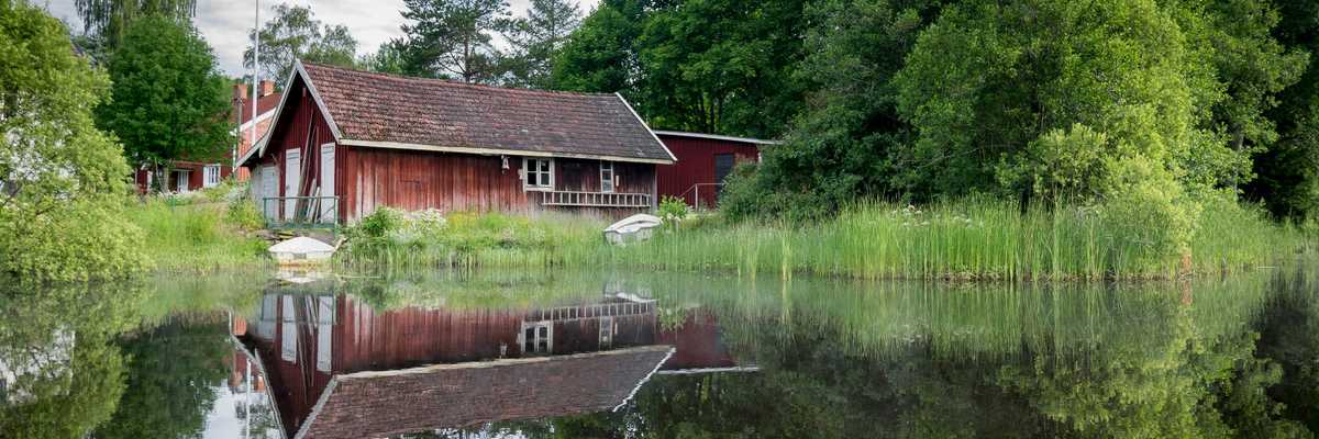 Red barn reflected in a calm pond with a green forest in the background.