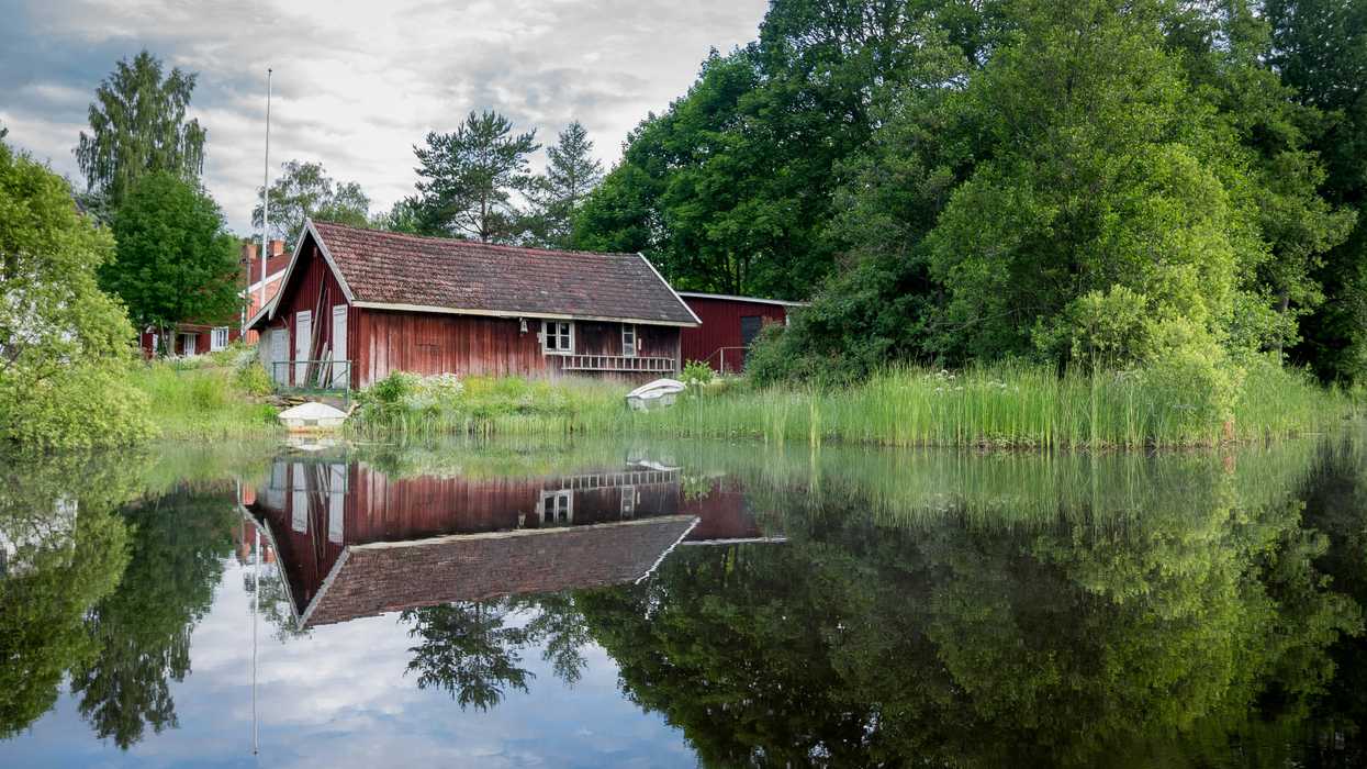 Red barn reflected in a calm pond with a green forest in the background.