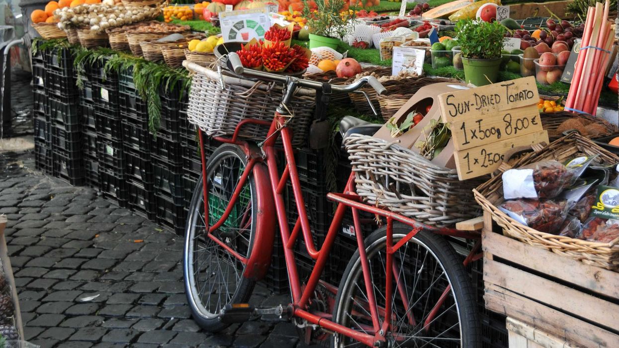 Red bicycle in front of a fruit and vegetable stand.