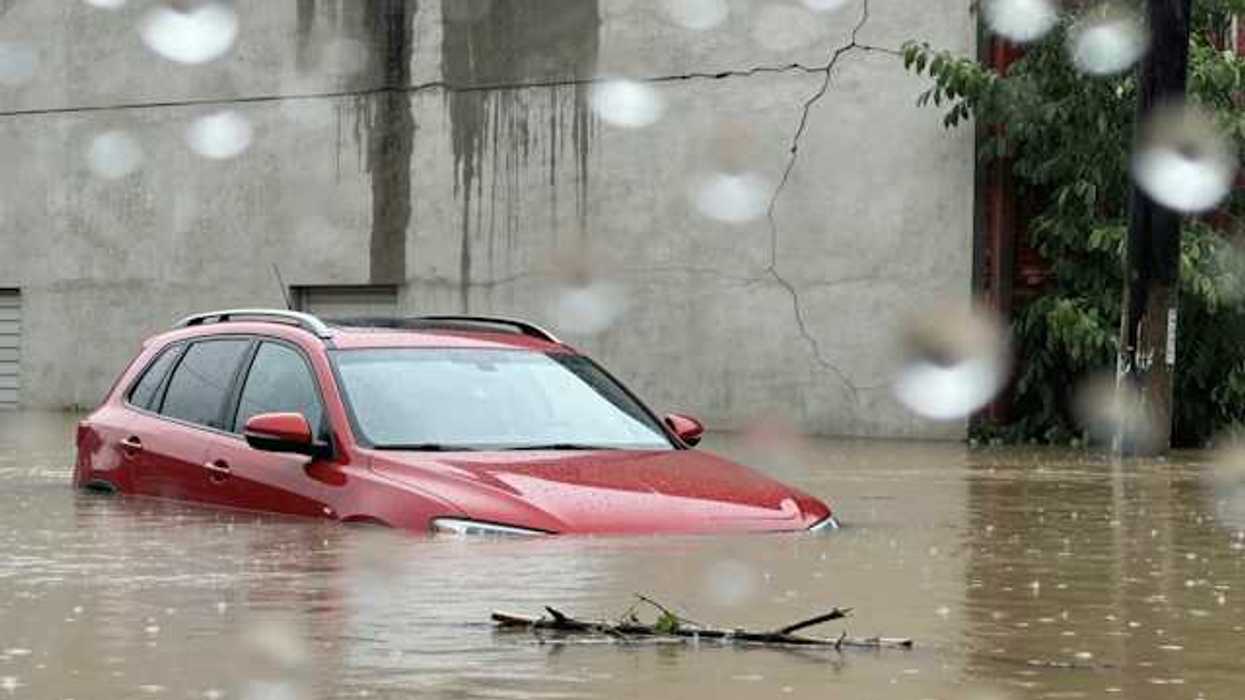 Red car submerged under flood waters with a concrete building behind it