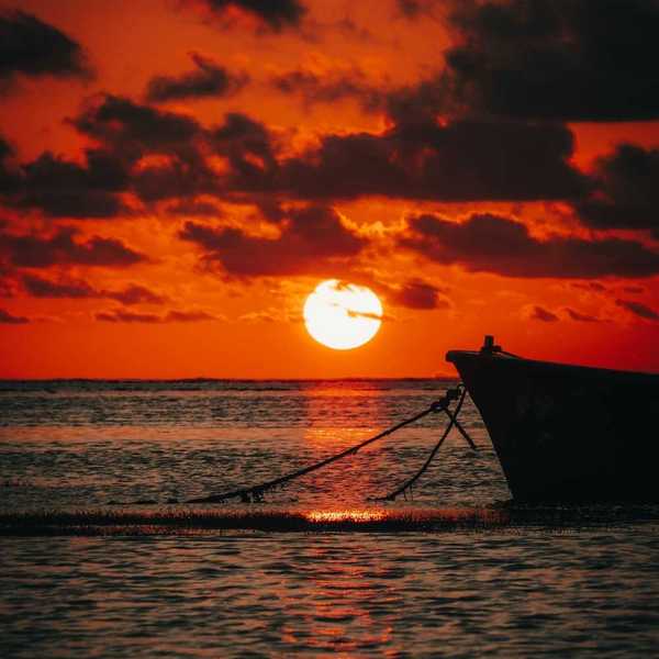 Red sunset over the ocean backlighting a tied-off skiff