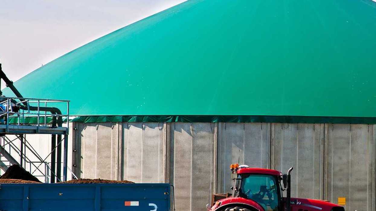 Red tractor hitched to a wagon of manure parked in front of a biogas facility.