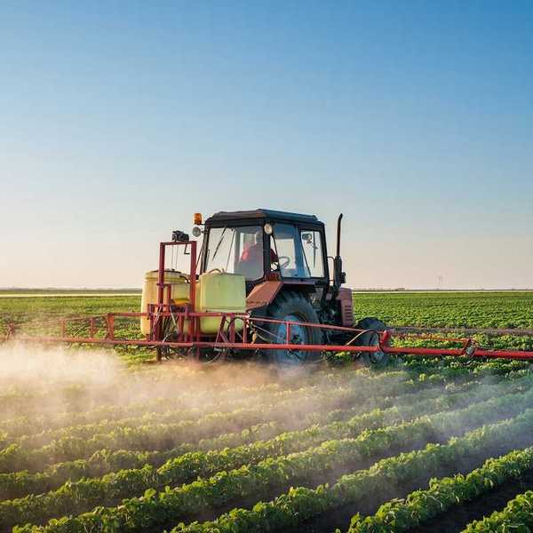 Red tractor mounted with equipment spraying herbicides onto row crops