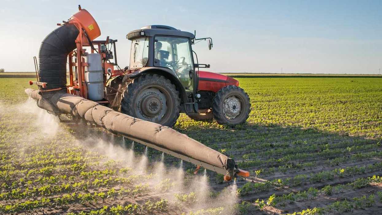 Red tractor pulling pesticide application equipment and applying pesticides to soybeans