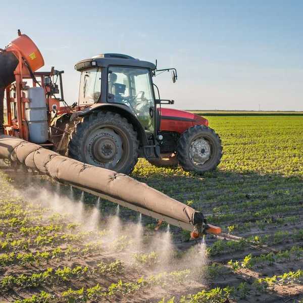 Red tractor pulling pesticide application equipment and applying pesticides to soybeans
