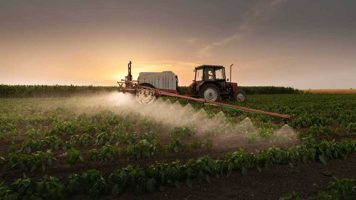 Red tractor pulling spraying equipment and applying pesticides or herbicides