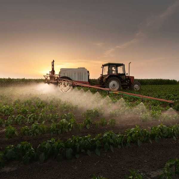 Red tractor pulling spraying equipment and applying pesticides or herbicides