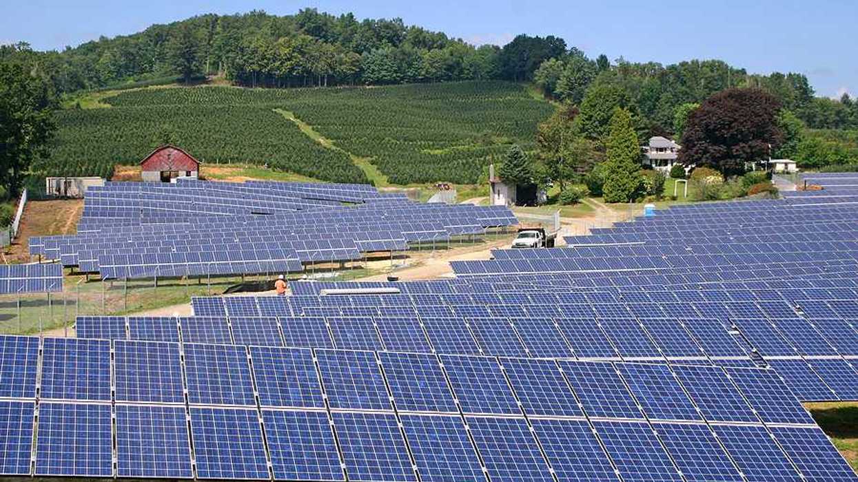 Rows of solar panels stretching up a hill toward a farm field