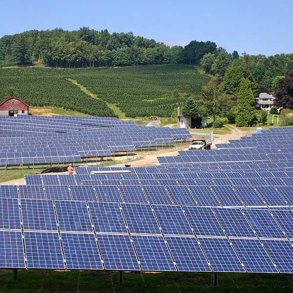 Rows of solar panels stretching up a hill toward a farm field