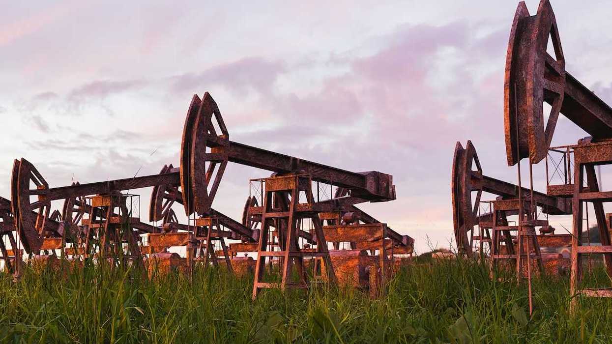 Rusted and abandoned oil pumps with grass growing around it against sunset.