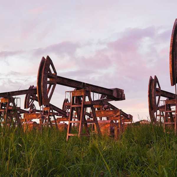 Rusted and abandoned oil pumps with grass growing around it against sunset.