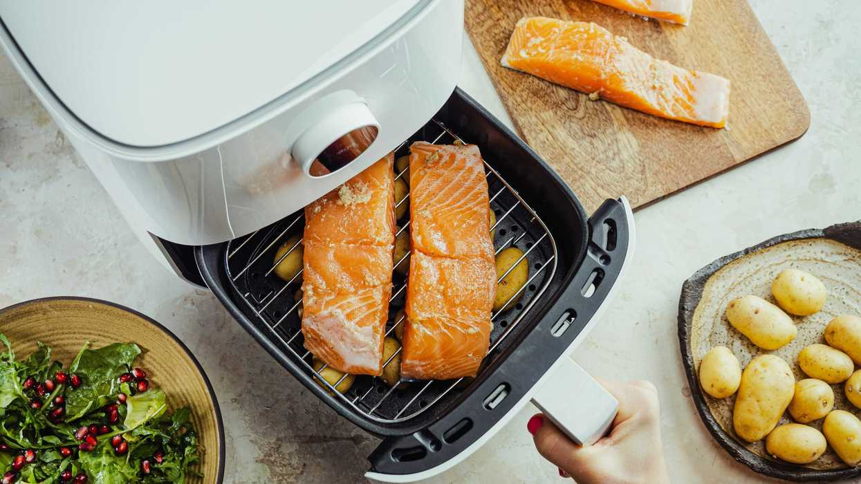 Salmon on a grill in an air fryer surrounded by plates of potatoes and salad.